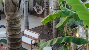 A hammock hanging between palm trees, a wooden bench, and a dining table with chairs in a tropical garden setting. - B&B L'Antica Rimessa (Lecce)