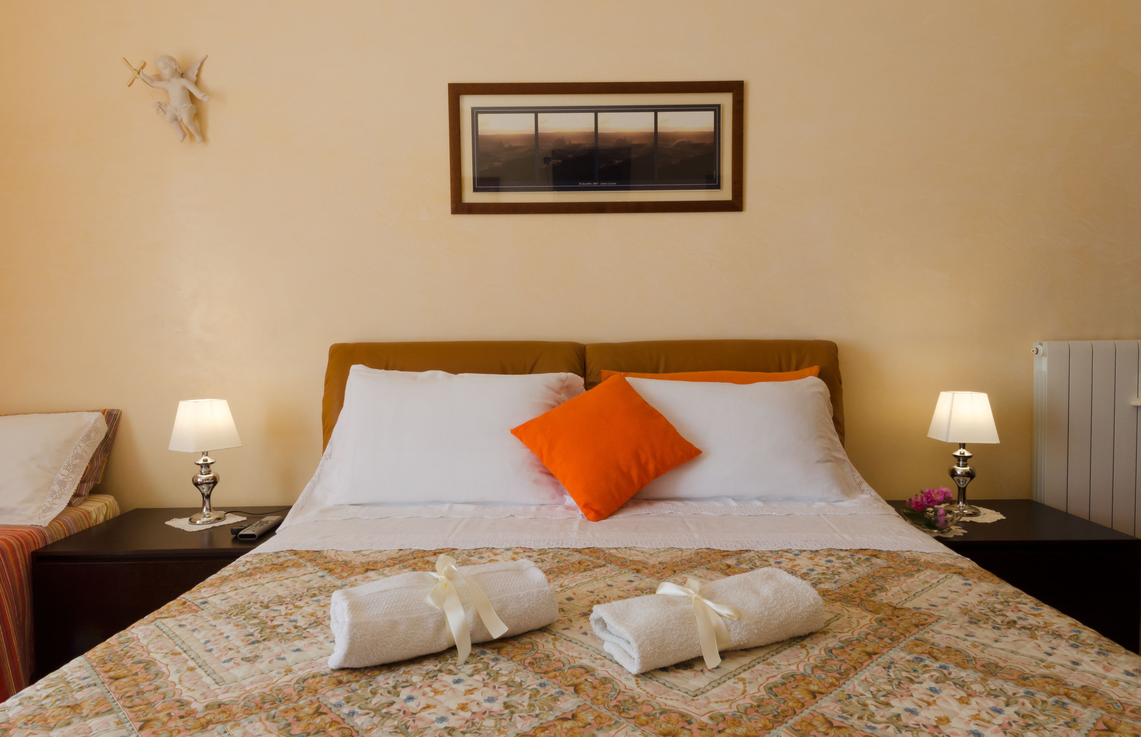 A neatly made bed with white and orange pillows, two bedside lamps, and a framed picture on the wall.