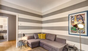 A modern living room with a grey sectional sofa, a small round table, a floor lamp, and a colorful abstract painting on the wall. - Cinque Terre Decor (La Spezia)