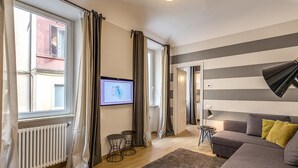 A living room with a grey sofa, a TV on the wall, a radiator, and a window with curtains. - Cinque Terre Decor (La Spezia)