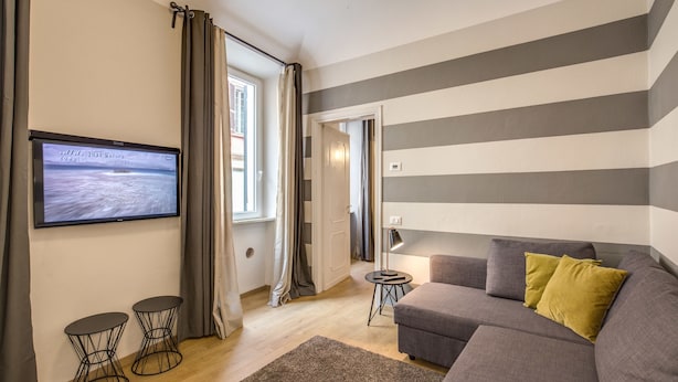 A modern living room with a grey sofa, a flat-screen TV mounted on the wall, and a small side table. - Cinque Terre Decor (La Spezia)