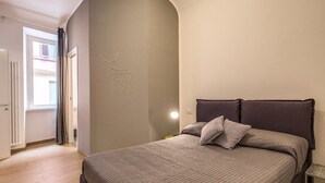 A bedroom with a bed, a headboard, a wall-mounted light, and a door leading to another room. - Cinque Terre Decor (La Spezia)