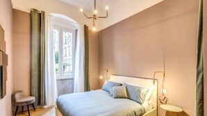 Une chambre à coucher comprenant un lit, une chaise, une table de chevet et une fenêtre avec des rideaux.