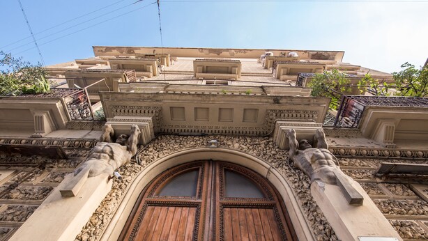 Une entrée imposante, avec une porte en bois, des sculptures complexes en pierre et une enseigne indiquant le nom et l’adresse.