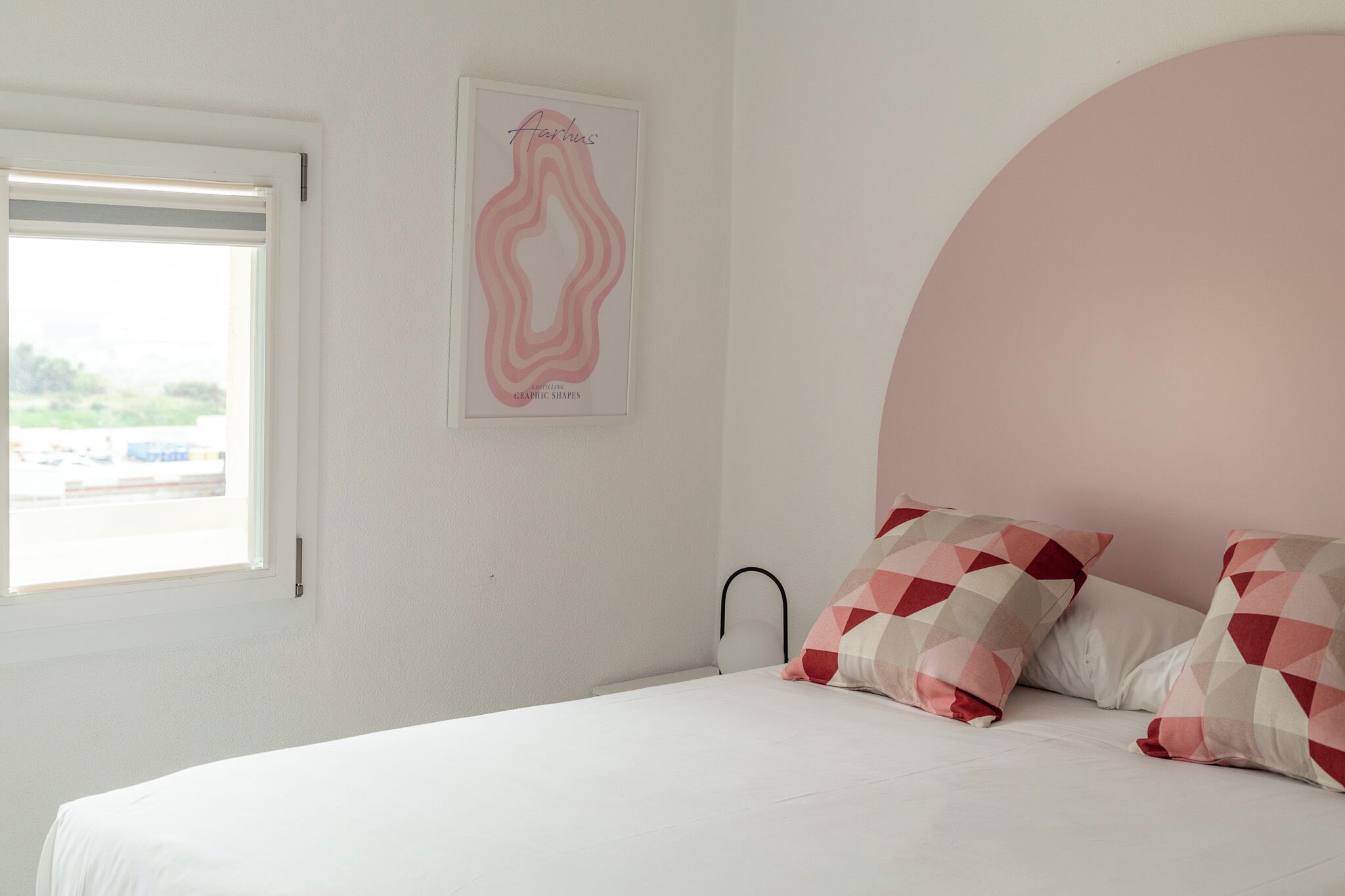 Un dormitorio con cama, un ventanal grande y una obra de arte colgada en la pared.