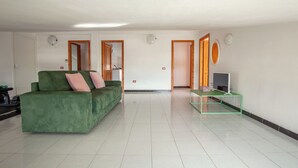 A spacious living area with a green sofa, a small green table, and a television on a stand. - Spacebility Airport-  self check-in (Cagliari)