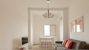 A living room with a sofa, TV, and a dining table with chairs. - Spacebility Airport-  self check-in (Cagliari)