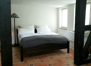 Una cama con ropa de cama blanca en una habitación con piso de baldosas y un radiador.