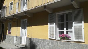 A yellow building with white shutters and a stone base. - Palazzo Colombino B&B (Giaveno)