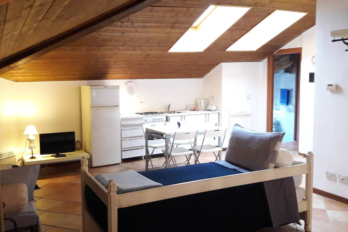 A compact room with a bed, a desk with a computer, a small kitchenette, and a window.