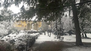 Un patio cubierto de nieve con una estatua, árboles y un edificio al fondo.