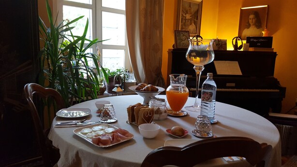 Mesa de comedor lista con comida, bebidas y un piano al fondo.