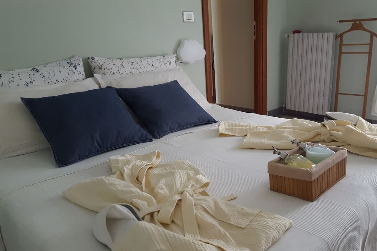 A neatly made bed with a floral pillow set, a dark blue pillow, and a wooden side table with a bottle and a container.