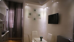A modern kitchen with white cabinets, a dining table with chairs, a flat-screen TV mounted on the wall, and a window with curtains. - Blanco Vaticano (Rome)