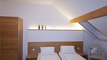 A bedroom with two beds, a wooden wardrobe, a chair, and a skylight.
