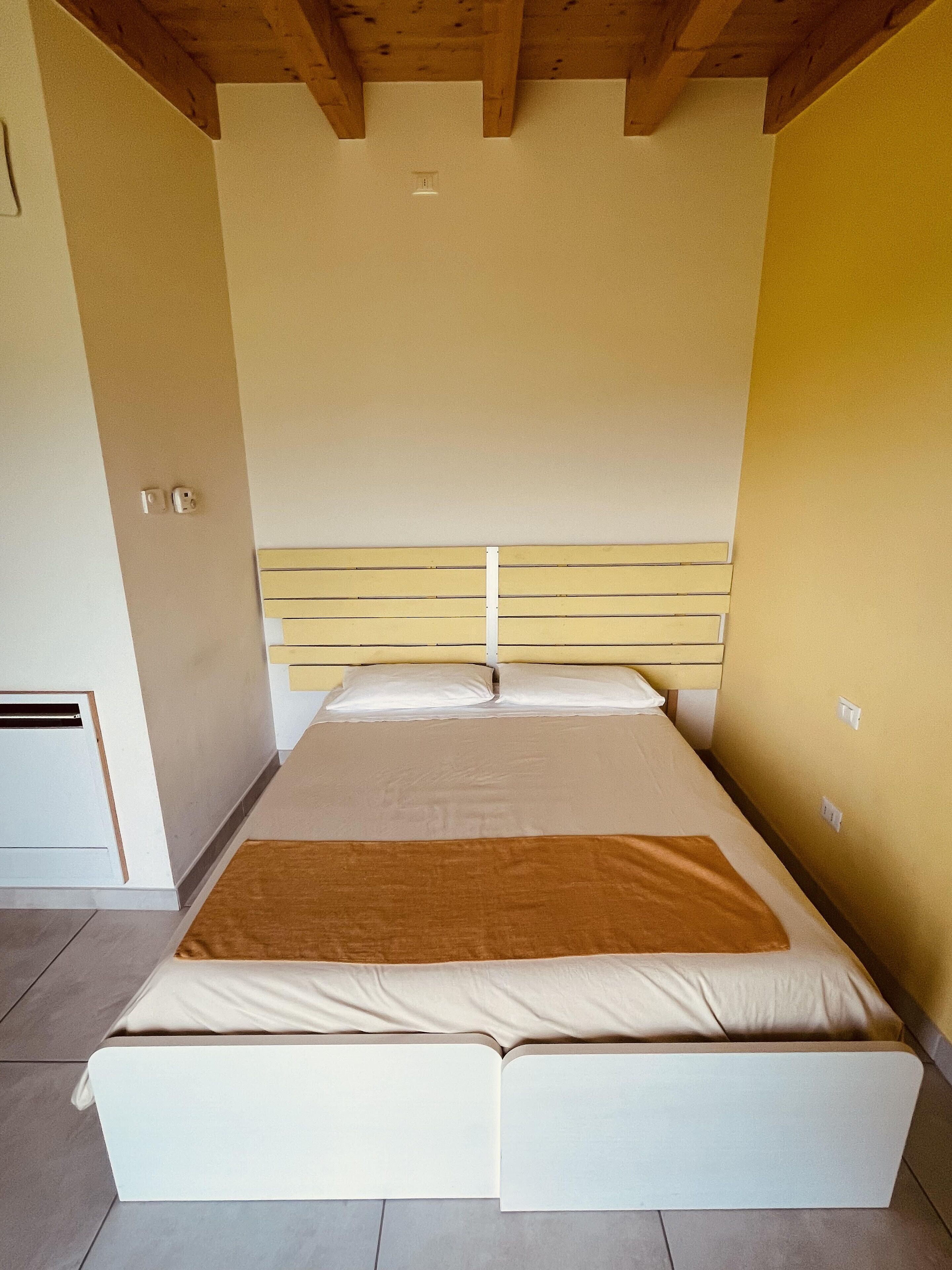 Una cama individual con cabecera de madera en una habitación con paredes lisas y suelo de baldosas.