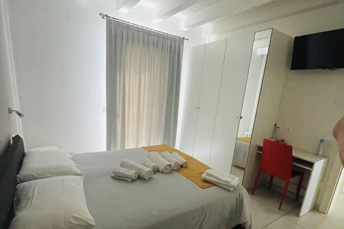 A hotel room with a bed, a desk, a chair, a television, and a wardrobe.