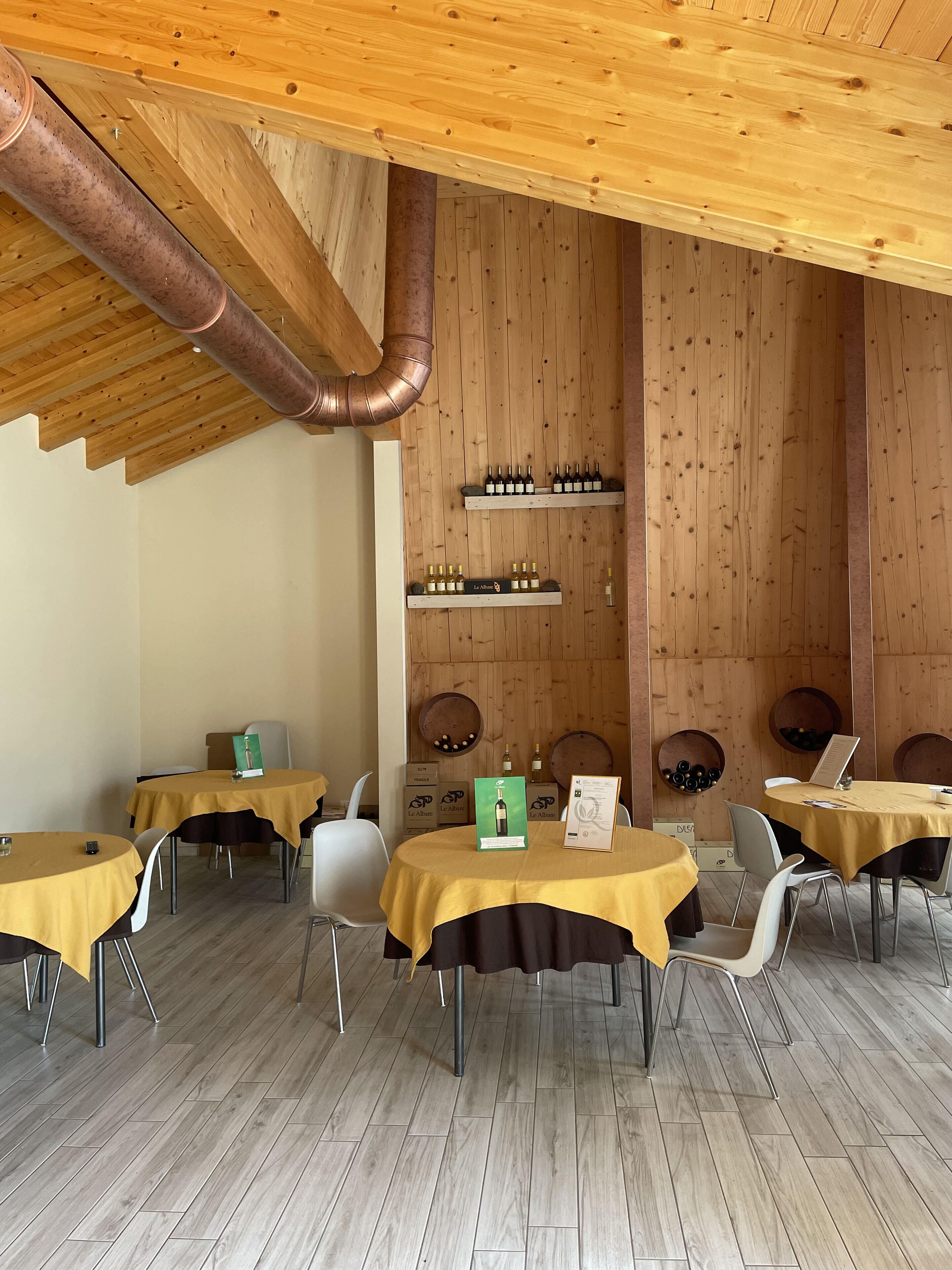 Un restaurante con paredes y techo de madera, mesas con manteles amarillos y botellas de vino en estantes.