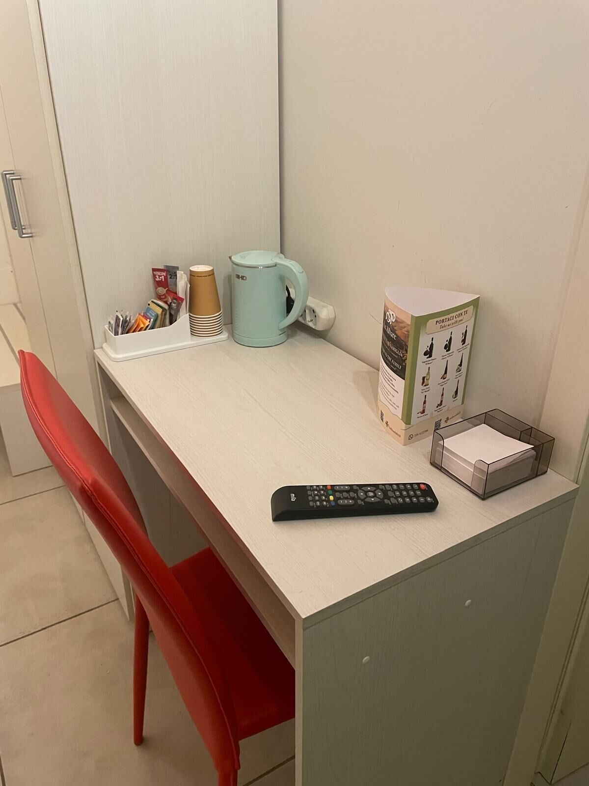 Un pequeño escritorio con un control remoto, una taza, una caja de pañuelos y un dispensador de pañuelos.