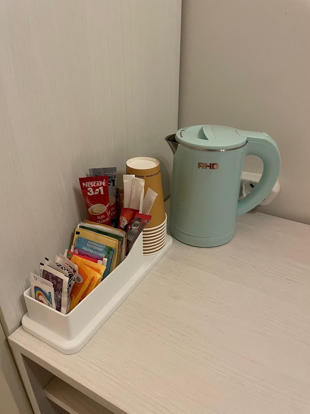 A shelf with a coffee maker and a container holding coffee pods and a stack of disposable cups.