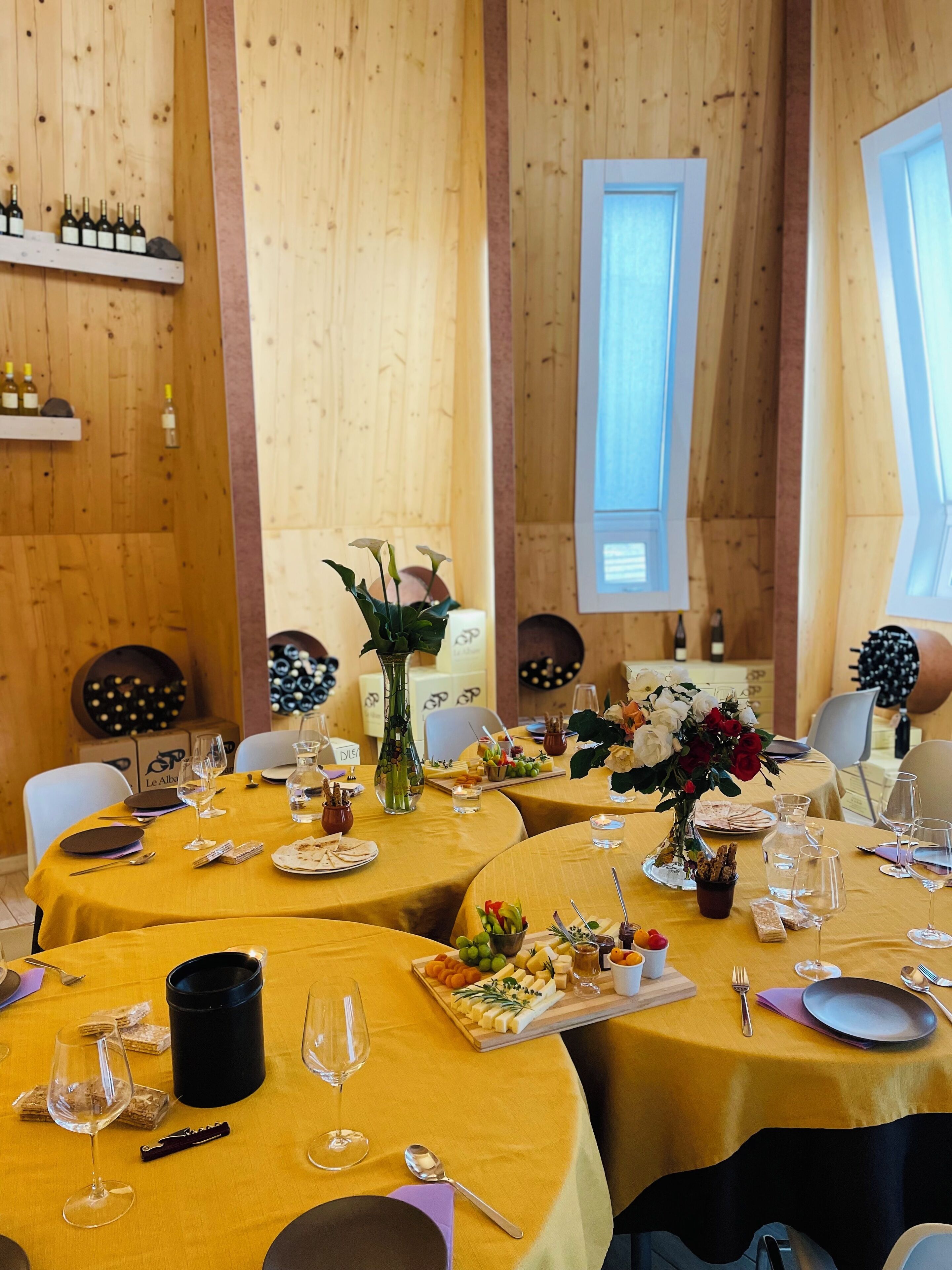 Un restaurant doté de plusieurs tables rondes recouvertes de nappes jaunes, chacune agrémentée de verres à vin, d’assiettes et d’une variété d’amuse-gueules.