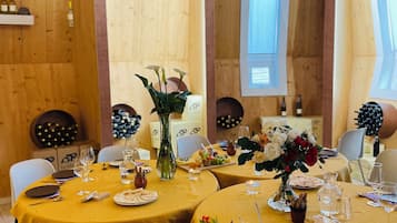 Un restaurante con varias mesas redondas cubiertas con manteles amarillos, cada una dispuesta con copas de vino, platos y una variedad de aperitivos.