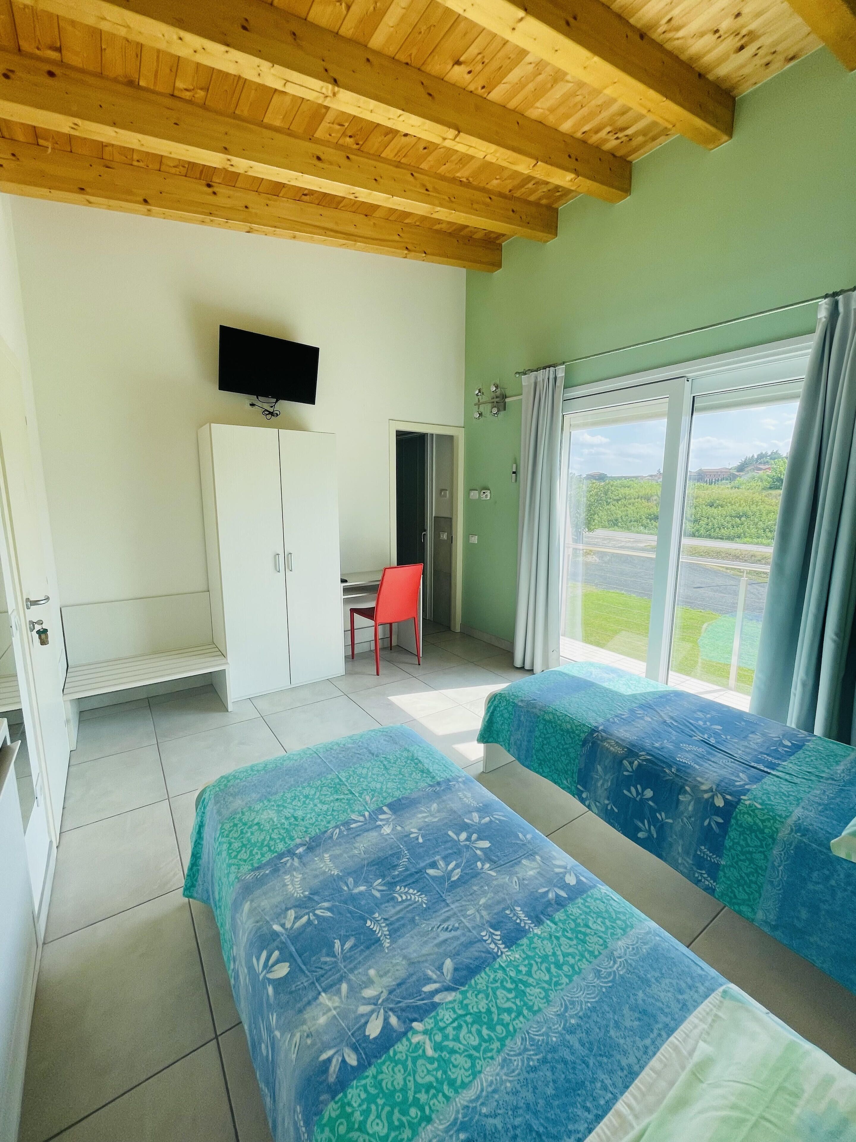 Una habitación con dos camas, un televisor montado en la pared, un armario y una ventana con cortinas.