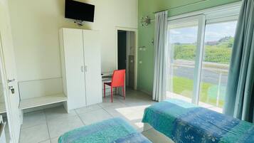 Una habitación con dos camas, un televisor montado en la pared, un armario y una ventana con cortinas.