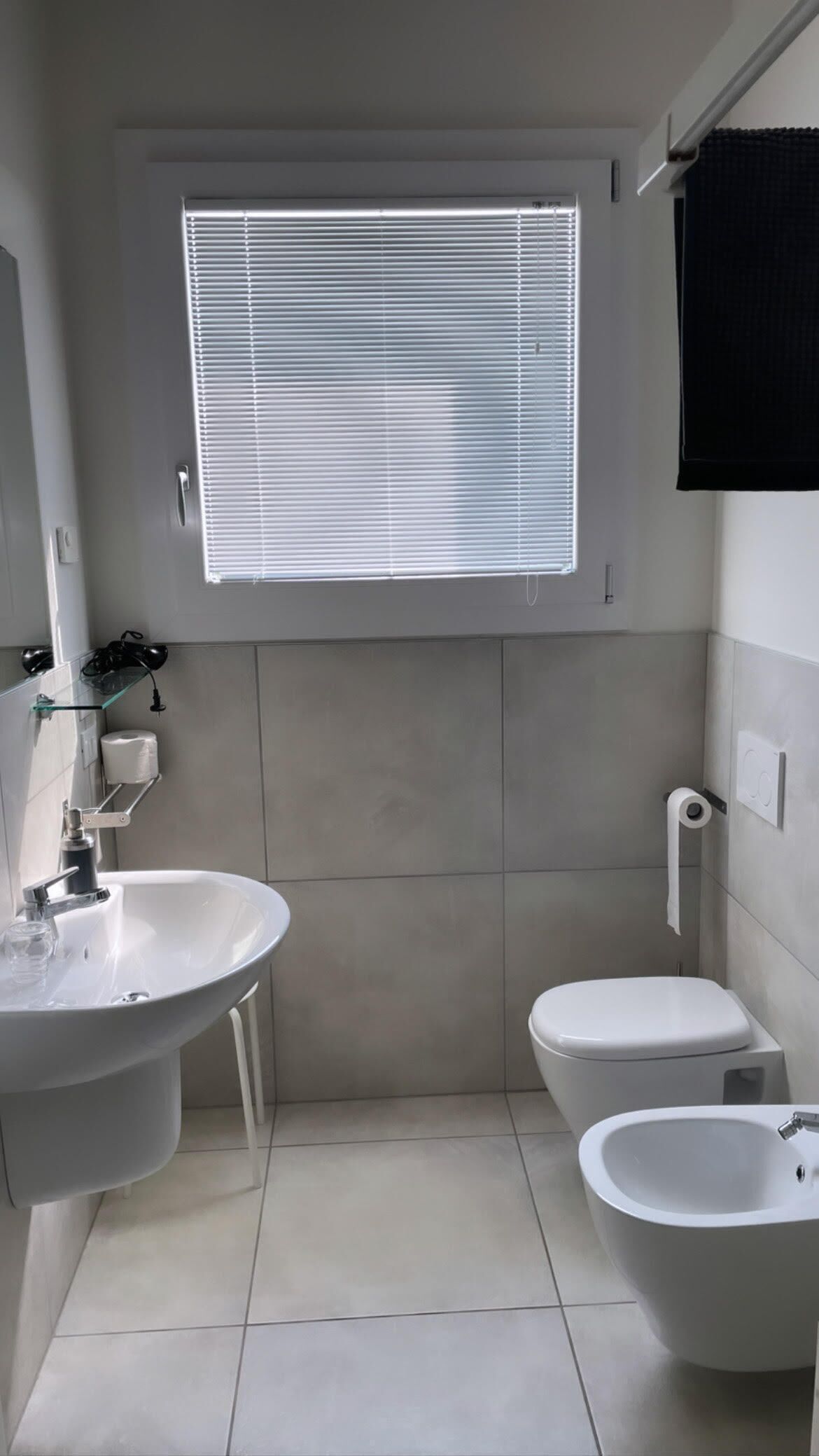 A compact bathroom with a sink, toilet, and bidet, featuring a window with blinds.