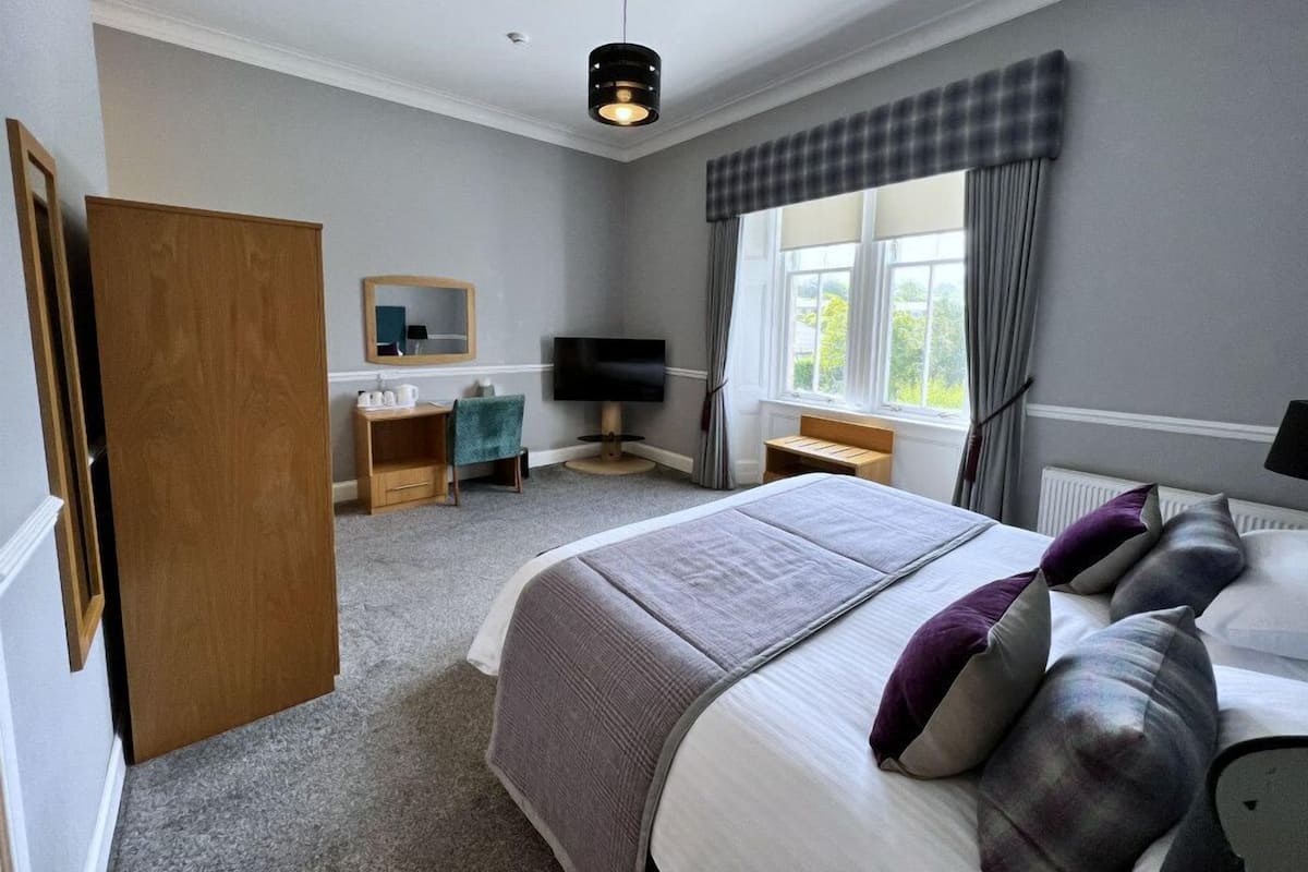 A hotel room with a bed, a desk, a TV, a wardrobe, and a window with curtains.