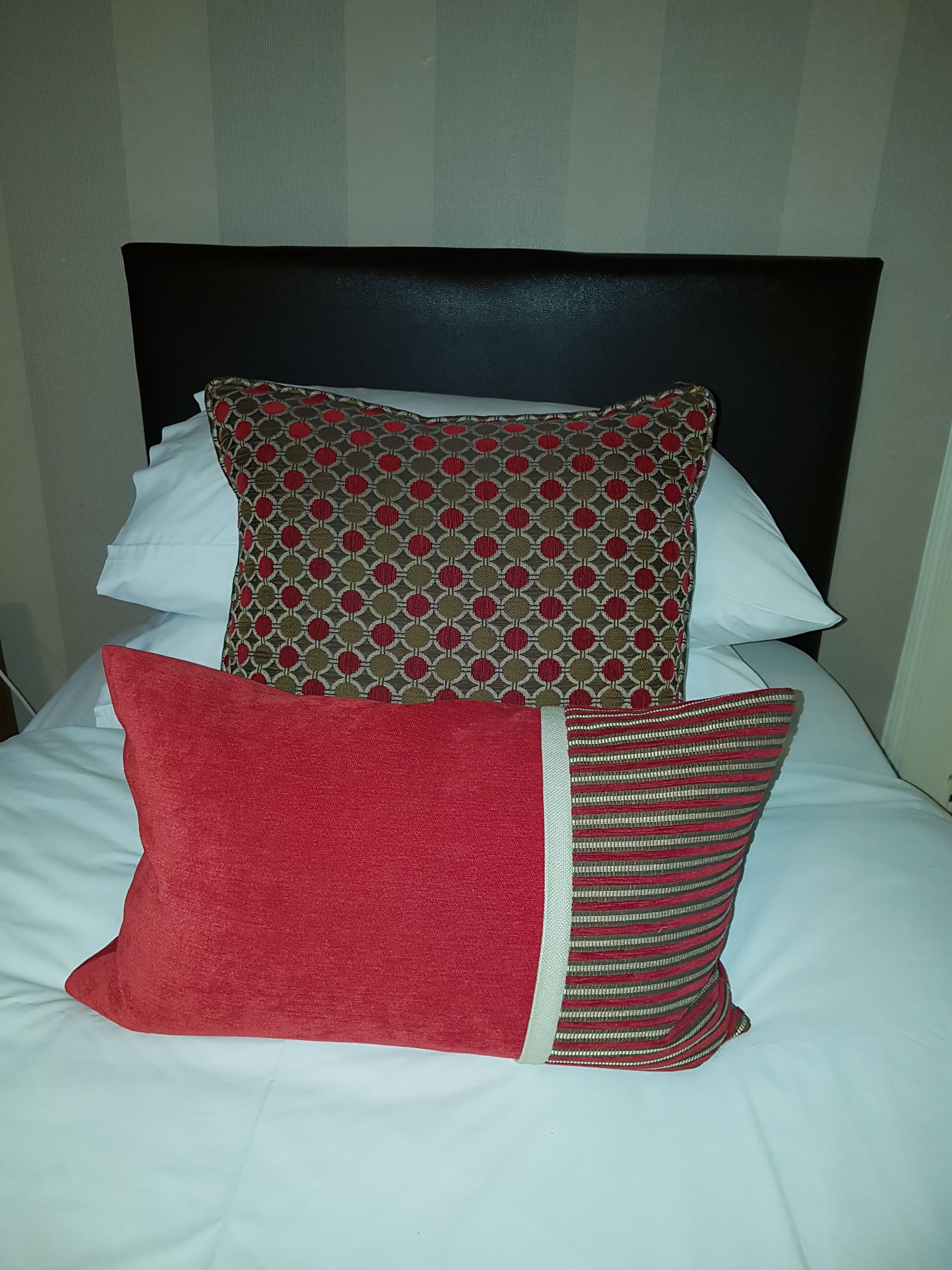 Un lit avec une tête de lit noire, des oreillers blancs et un coussin rouge.