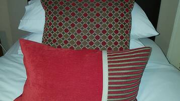 Un lit avec une tête de lit noire, des oreillers blancs et un coussin rouge.