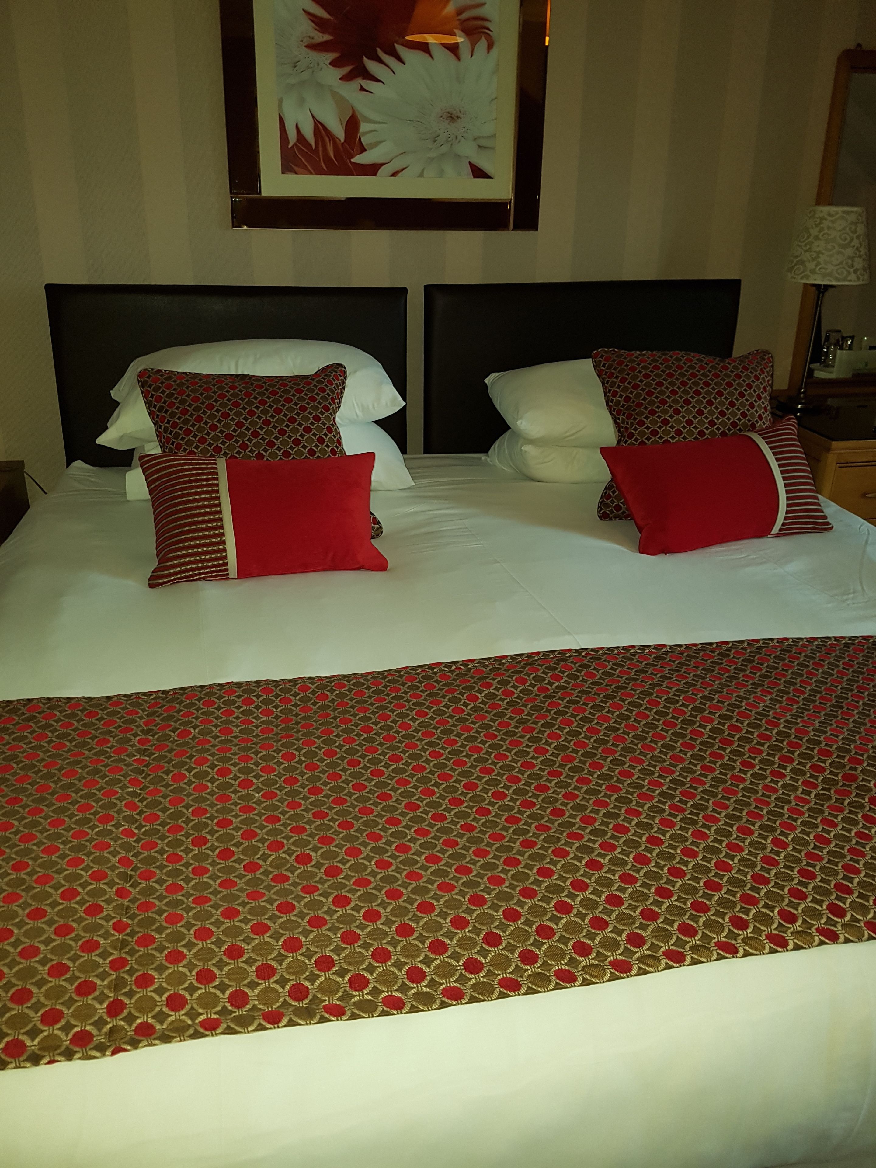 A neatly made bed with a patterned bedspread and two pillows, one with a red and white design and another with a red and beige pattern.