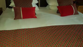 A neatly made bed with a patterned bedspread and two pillows, one with a red and white design and another with a red and beige pattern.
