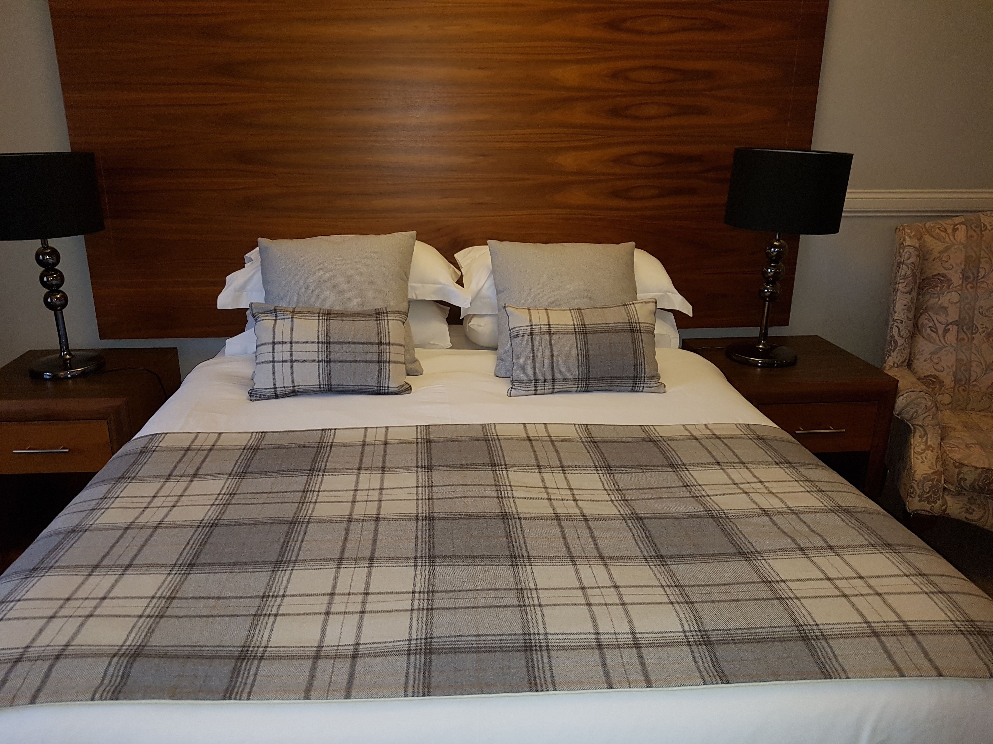 A hotel room with a large bed, two nightstands, a wooden headboard, and a chair.