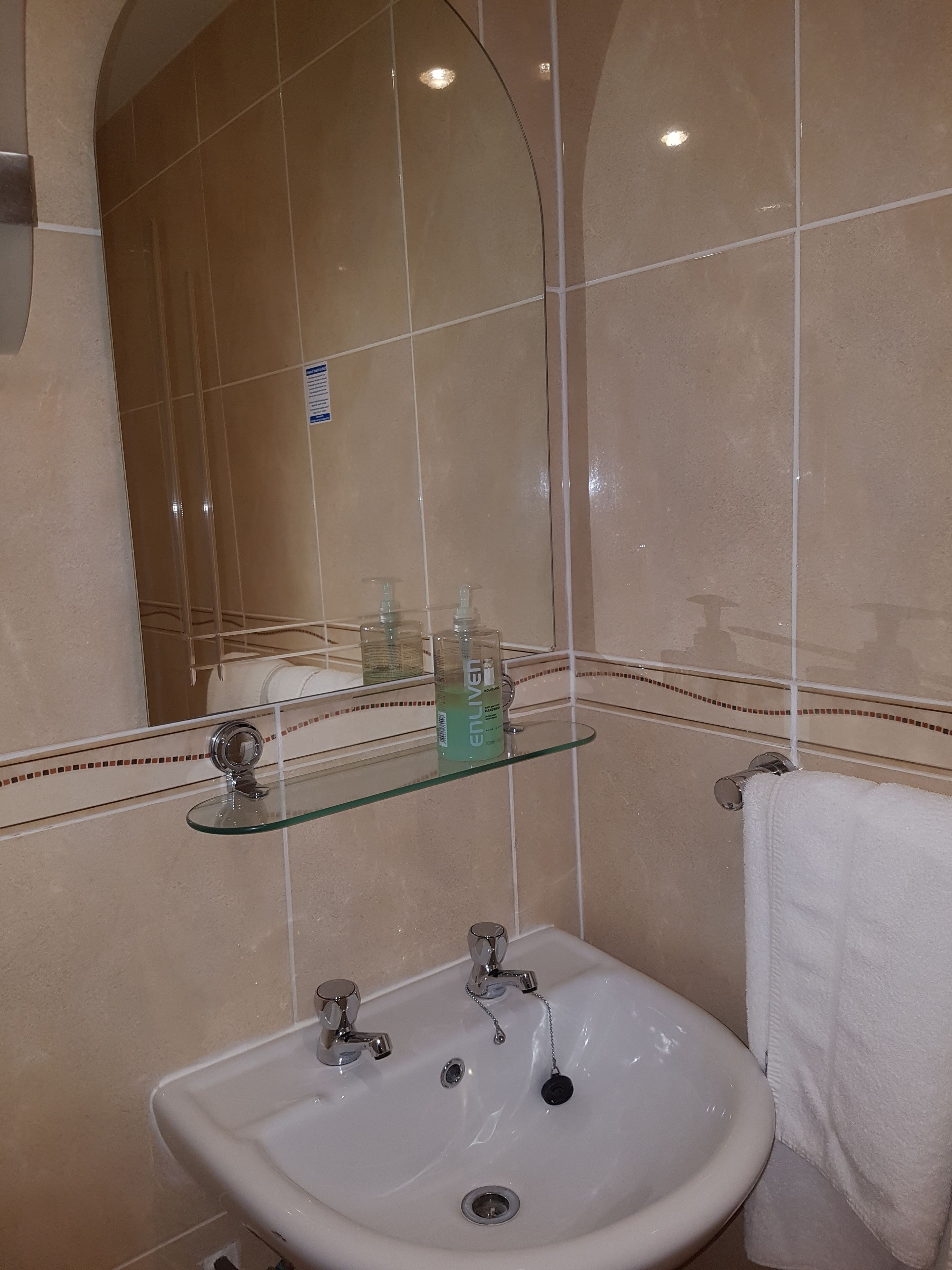 A bathroom with a white sink, a glass shelf with toiletries, and a towel hanging on the wall.