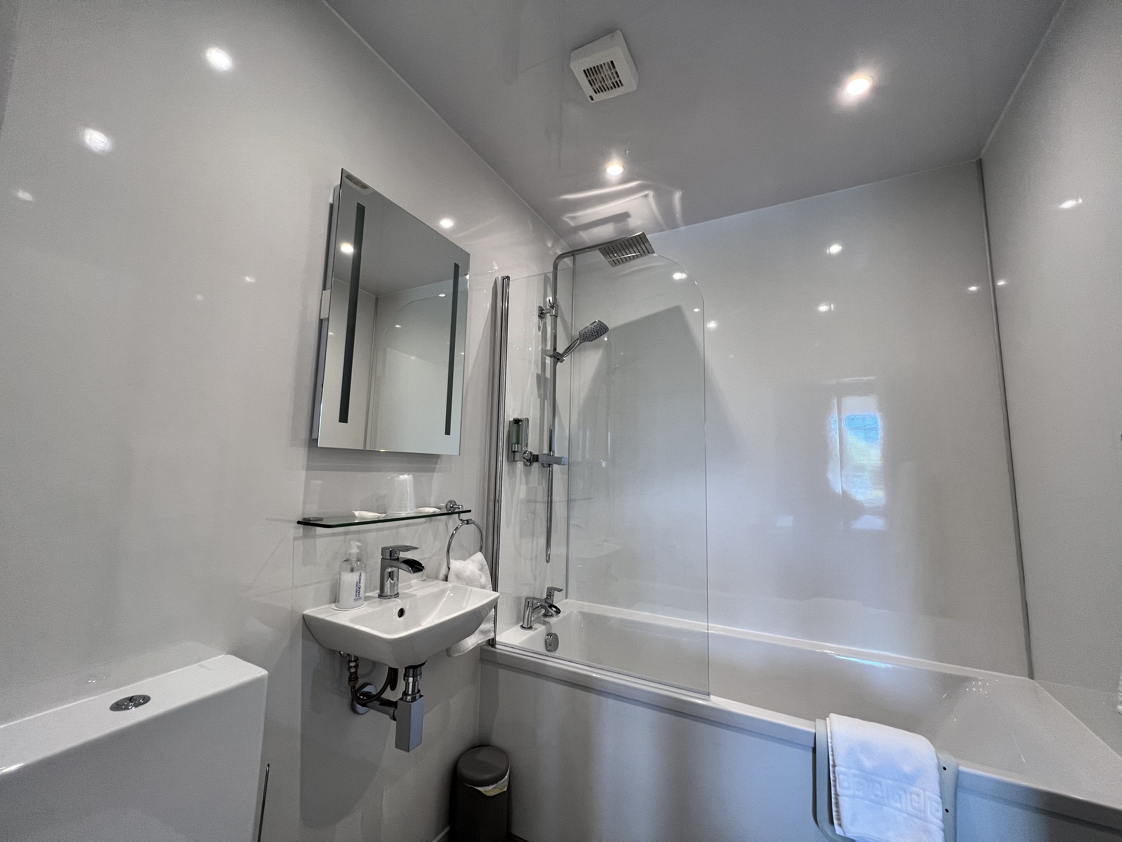 Un baño moderno con cabina de ducha de vidrio, un lavabo con espejo y un perchero para toallas.