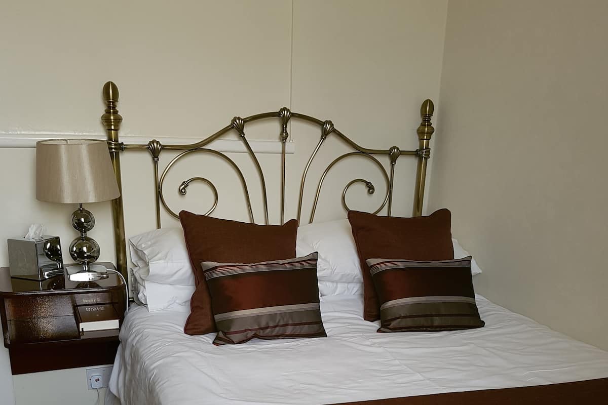 A hotel room with a bed, a nightstand, a lamp, and a power outlet.