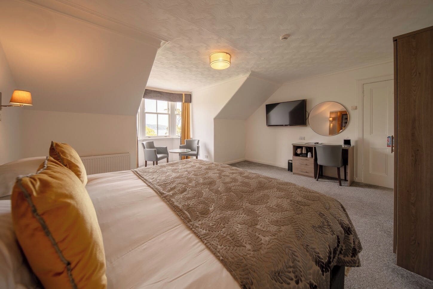 A bedroom with a bed, a desk, a chair, a TV, and a window.