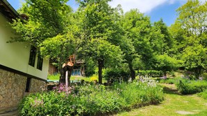 A garden with a stone wall, a wooden chair, and a variety of flowering plants. - Little River Guest House (Gabrovo)