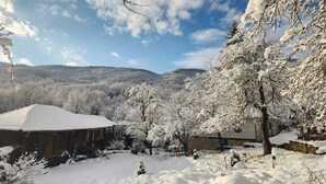 A snow-covered landscape with a building that has a sloped roof and a stone wall. - Little River Guest House (Gabrovo)