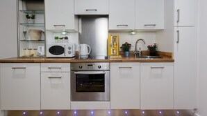 A modern kitchen with white cabinets, stainless steel appliances, and a wooden countertop. - Live in Leeds Sky Penthouse (Leeds)