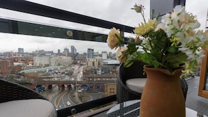 A balcony with a view of a cityscape, a wicker chair, and a potted plant. - Live in Leeds Sky Penthouse (Leeds)
