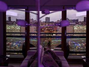 A room with a view of a cityscape, featuring modern buildings and a busy street with buses. - Live in Leeds Sky Penthouse (Leeds)