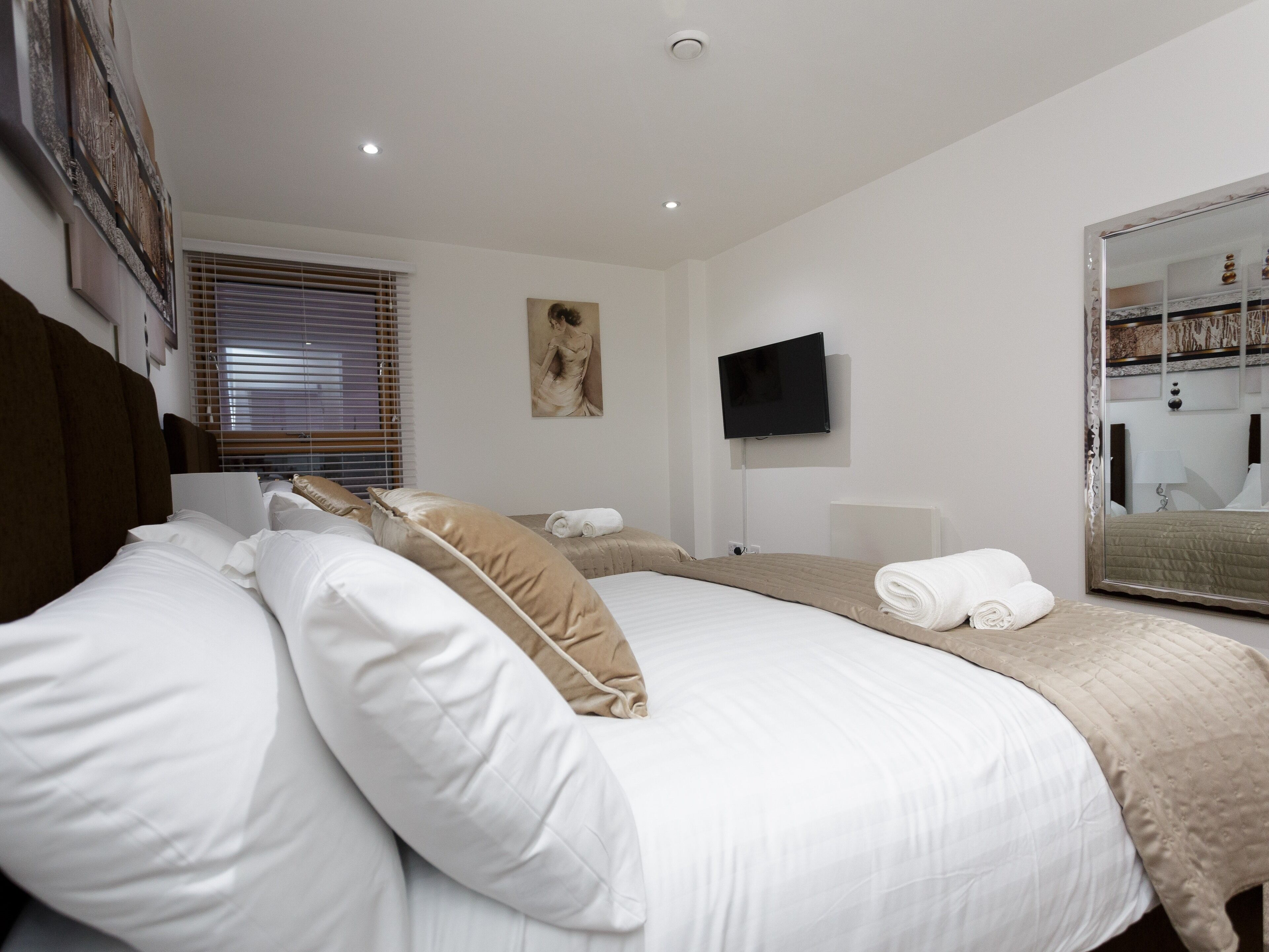A hotel room with a large bed, a TV mounted on the wall, and a mirror reflecting the room.