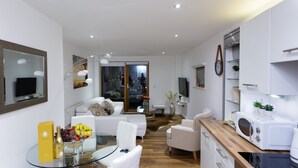 A modern living room with a glass dining table, white sofas, and a kitchen area with a microwave and oven. - Live in Leeds Sky Penthouse (Leeds)