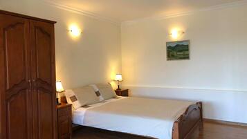 Une chambre à coucher avec un lit en bois, deux tables de chevet avec des lampes, une armoire en bois et un tableau représentant un paysage accroché au mur.