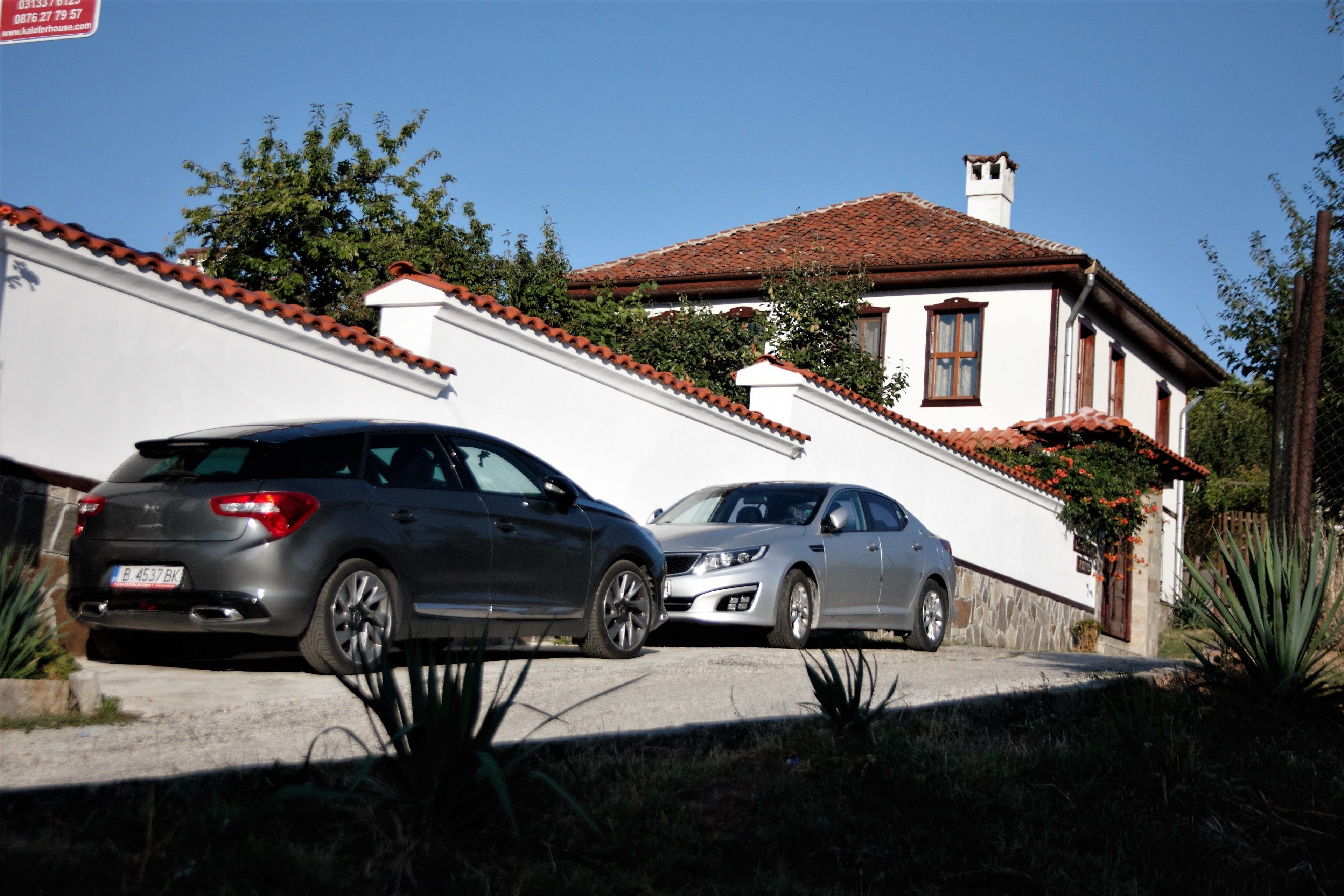 Two cars parked in front of a white building with a red-tiled roof.