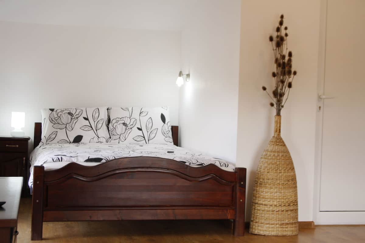 A bedroom with a wooden bed, a white wall, and a woven vase with dried flowers.
