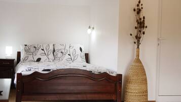 Un dormitorio con una cama de madera, una pared blanca y un jarrón tejido con flores secas.
